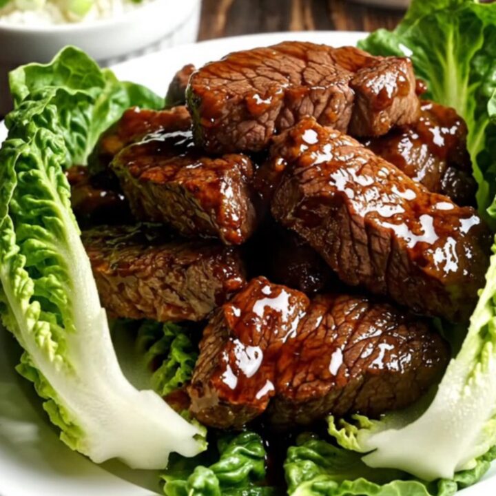 Close-up of caramelized Bulgogi steak tips being lifted from a black ceramic slow cooker with chopsticks.