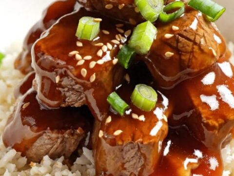 A black slow cooker filled with sticky honey-Sriracha steak bites glistening under warm kitchen light.
