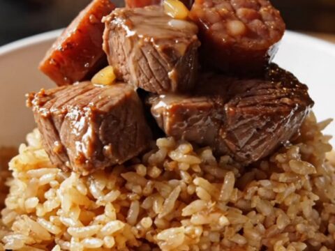 A close-up of tender Cajun steak bites and smoky Andouille sausage served in a bowl with a side of rice.