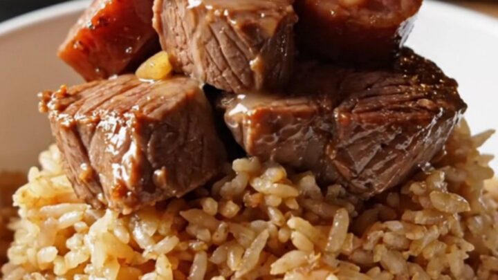 A close-up of tender Cajun steak bites and smoky Andouille sausage served in a bowl with a side of rice.