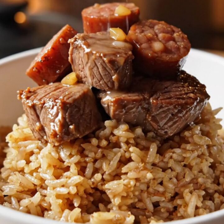 A close-up of tender Cajun steak bites and smoky Andouille sausage served in a bowl with a side of rice.