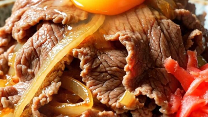 A close-up of a steaming bowl of Japanese Gyudon with tender beef, onions, and a vibrant egg yolk.