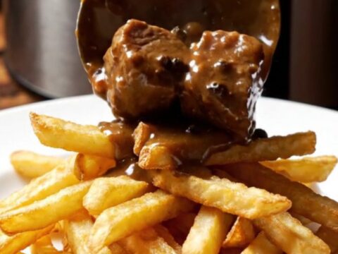 Close-up of tender steak bites in a creamy peppercorn brandy sauce in a ceramic slow cooker.