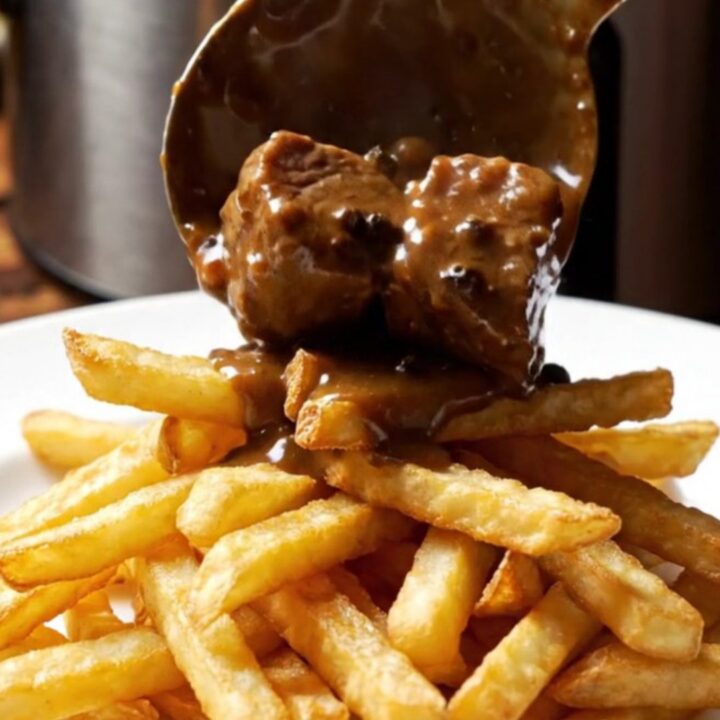 Close-up of tender steak bites in a creamy peppercorn brandy sauce in a ceramic slow cooker.