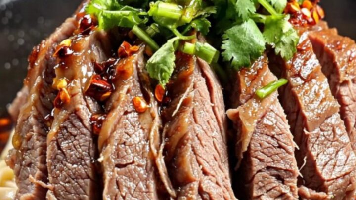 A close-up shot of tender, marbled beef shank slices in a dark, glossy, crimson Mala chili oil broth.