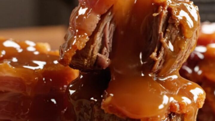 A close-up of bacon-wrapped steak bites glazed in a rich, shiny bourbon sauce on a dark platter.