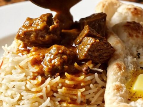 A close-up of a brass-trimmed slow cooker filled with vibrant, crimson Kashmiri beef Rogan Josh.