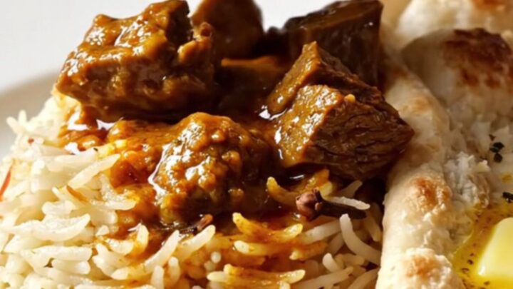 A close-up of a brass-trimmed slow cooker filled with vibrant, crimson Kashmiri beef Rogan Josh.