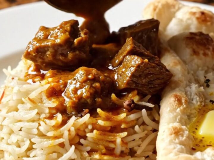 A close-up of a brass-trimmed slow cooker filled with vibrant, crimson Kashmiri beef Rogan Josh.