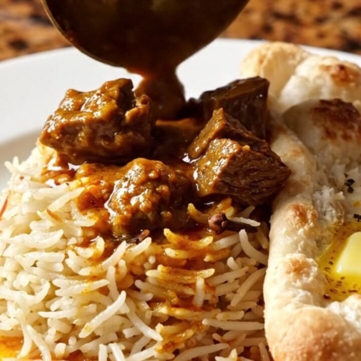 A close-up of a brass-trimmed slow cooker filled with vibrant, crimson Kashmiri beef Rogan Josh.