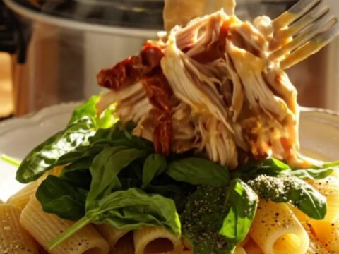 A close-up of creamy Crockpot sun-dried tomato chicken served over rigatoni pasta, garnished with fresh basil.