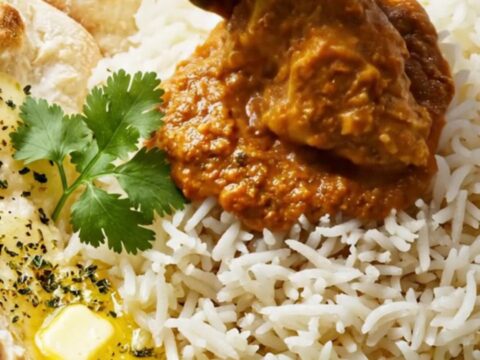 A ceramic slow cooker filled with creamy, vibrant orange-red butter chicken masala garnished with fresh cilantro.