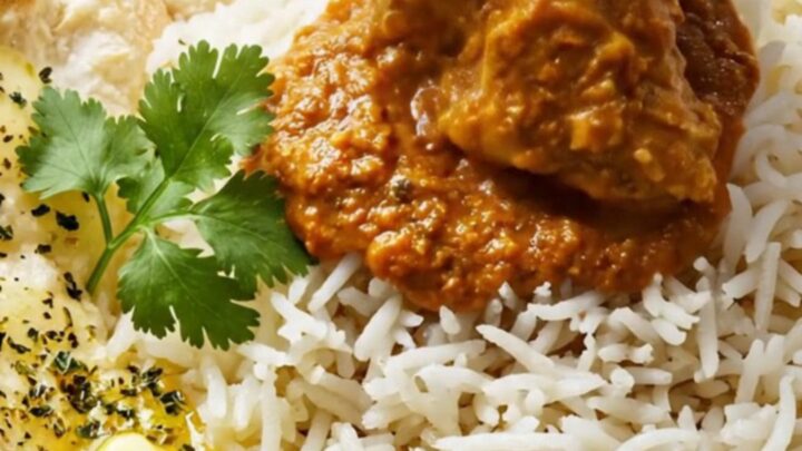 A ceramic slow cooker filled with creamy, vibrant orange-red butter chicken masala garnished with fresh cilantro.