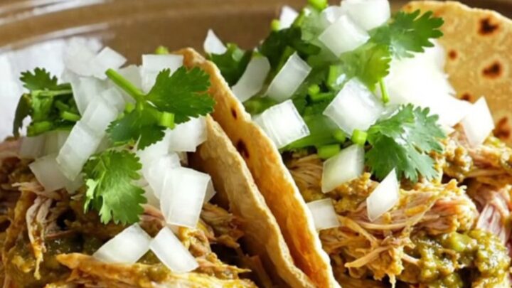 A close-up of shredded chicken in a creamy green salsa verde sauce served in warm corn tortillas with cilantro.