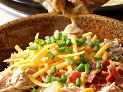 A creamy one-pot chicken and potato dish in a white slow cooker, topped with bacon and cheddar.