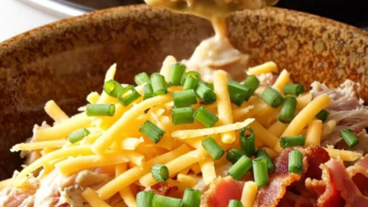 A creamy one-pot chicken and potato dish in a white slow cooker, topped with bacon and cheddar.