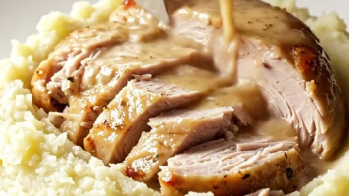 A golden-brown slow-cooked turkey breast served on a ceramic platter with fresh sage and rosemary.
