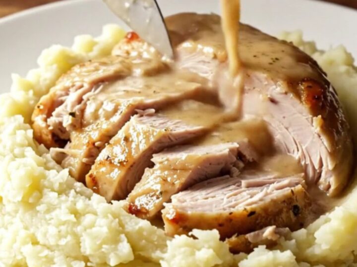 A golden-brown slow-cooked turkey breast served on a ceramic platter with fresh sage and rosemary.