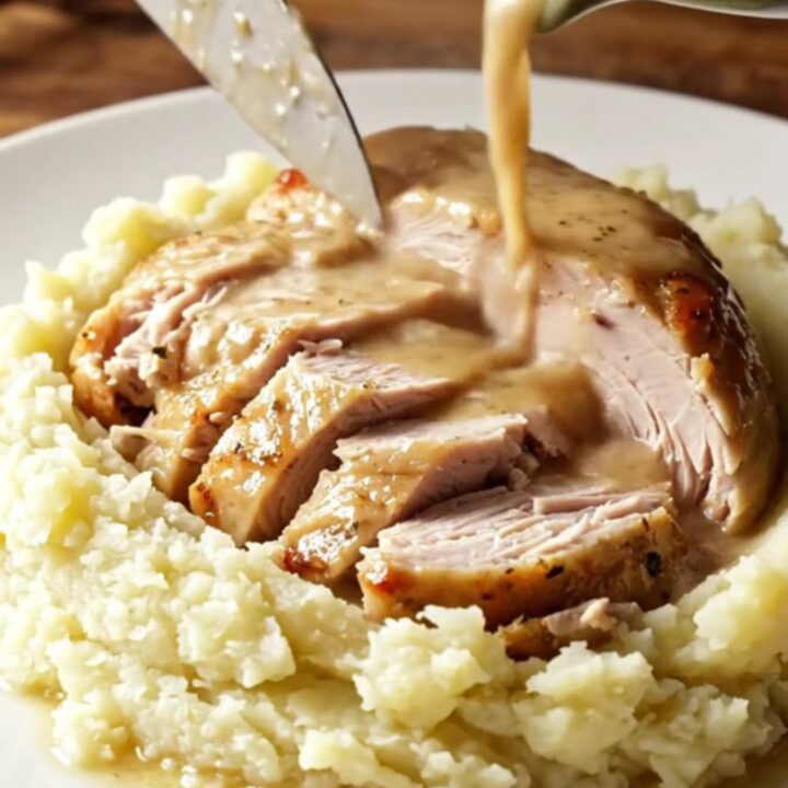 A golden-brown slow-cooked turkey breast served on a ceramic platter with fresh sage and rosemary.