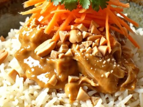 A close-up of creamy Thai peanut coconut chicken served over jasmine rice, garnished with peanuts and cilantro.
