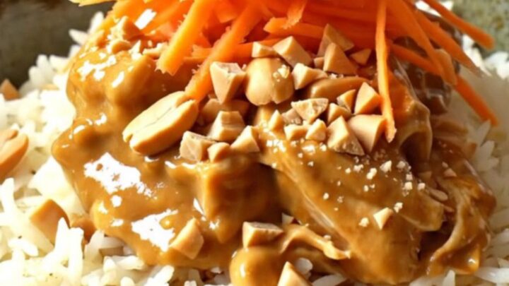 A close-up of creamy Thai peanut coconut chicken served over jasmine rice, garnished with peanuts and cilantro.