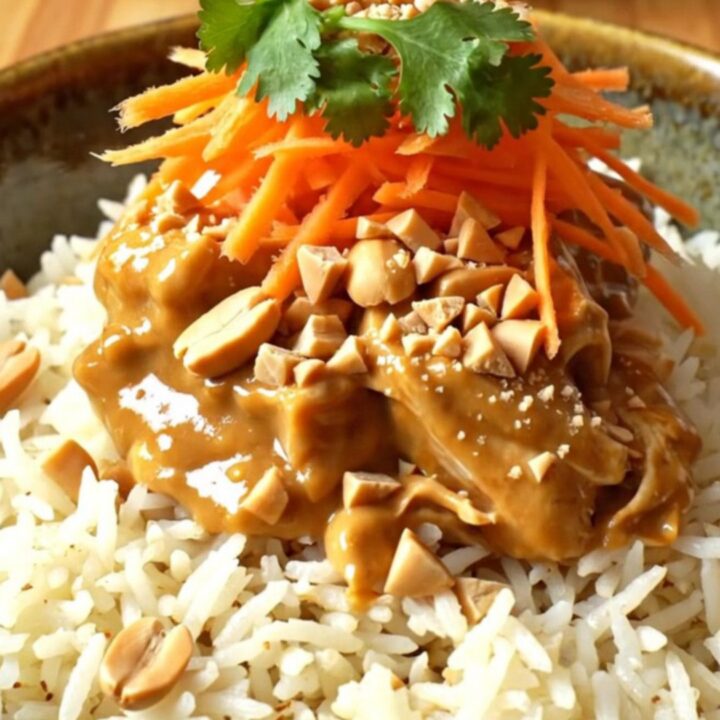 A close-up of creamy Thai peanut coconut chicken served over jasmine rice, garnished with peanuts and cilantro.