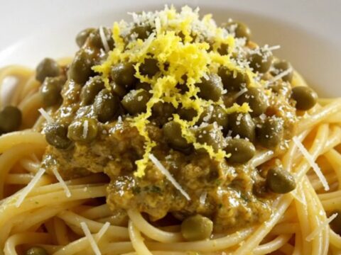 Tender shredded chicken in a glossy lemon garlic butter sauce with capers in a white ceramic slow cooker.