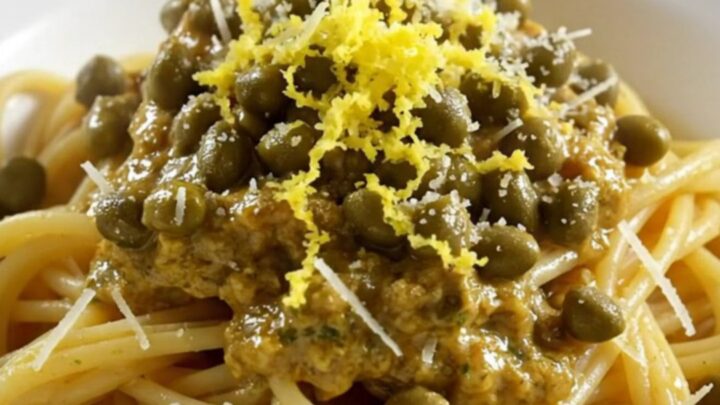 Tender shredded chicken in a glossy lemon garlic butter sauce with capers in a white ceramic slow cooker.