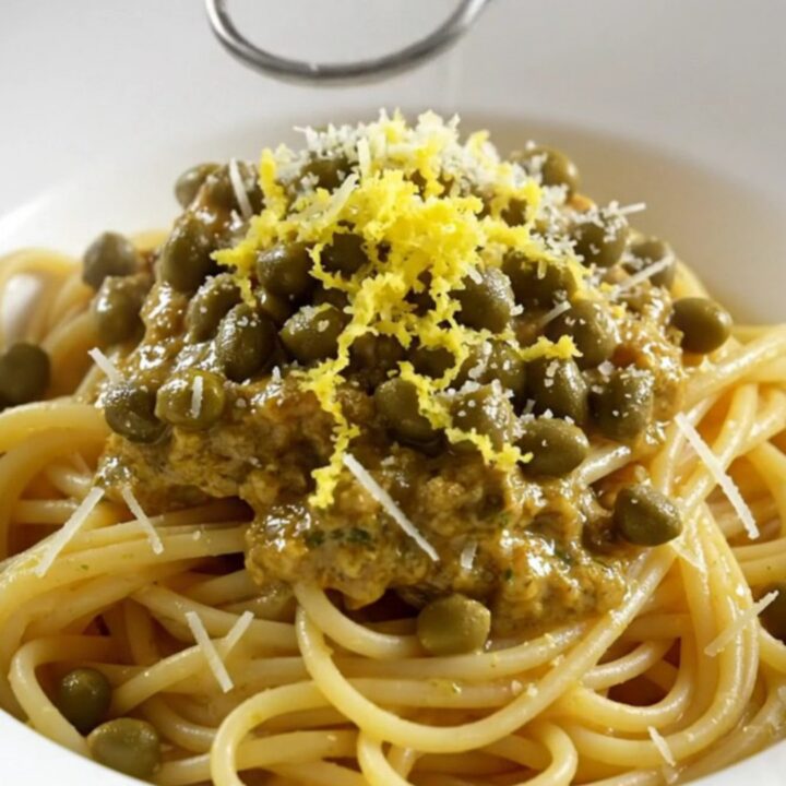 Tender shredded chicken in a glossy lemon garlic butter sauce with capers in a white ceramic slow cooker.