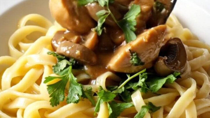 A close-up of creamy mushroom Marsala chicken served over buttery egg noodles in a rustic bowl.