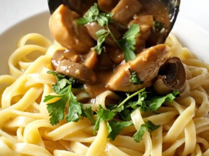 A close-up of creamy mushroom Marsala chicken served over buttery egg noodles in a rustic bowl.