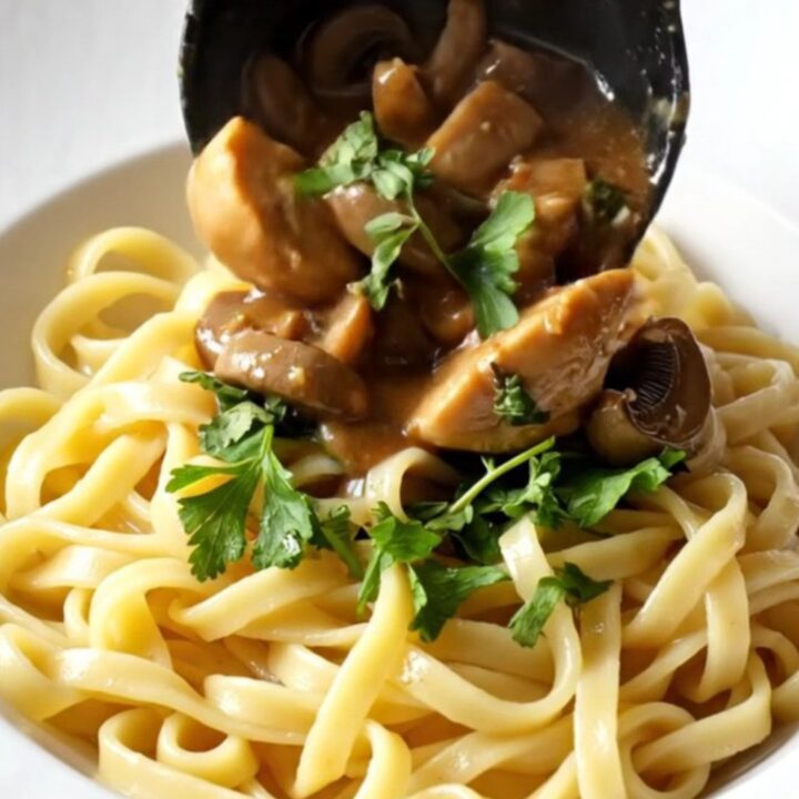 A close-up of creamy mushroom Marsala chicken served over buttery egg noodles in a rustic bowl.