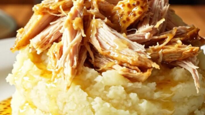 A close-up of shredded honey mustard rosemary chicken served over a mound of creamy mashed potatoes in a white bowl.