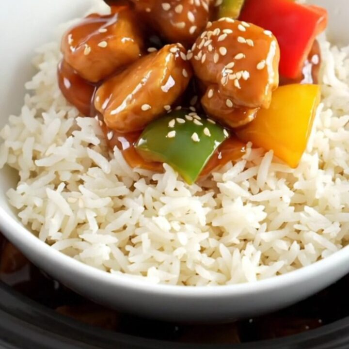 A glossy sweet and sour chicken dish with pineapple and peppers in a ceramic slow cooker.