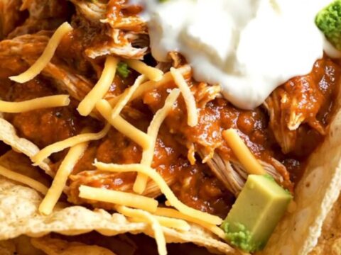 A close-up of creamy shredded chicken in a black slow cooker with melted cheese and red sauce.