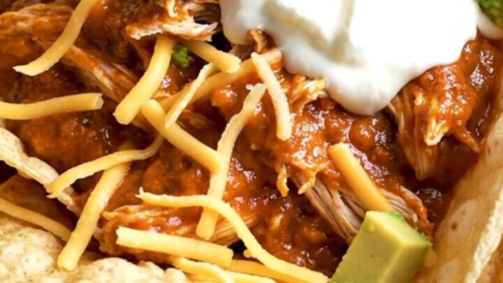 A close-up of creamy shredded chicken in a black slow cooker with melted cheese and red sauce.