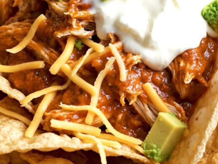 A close-up of creamy shredded chicken in a black slow cooker with melted cheese and red sauce.