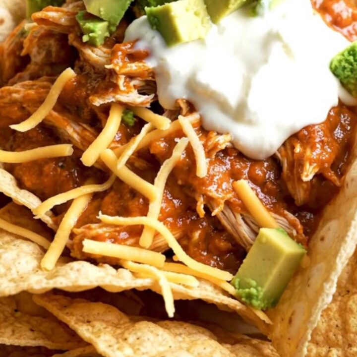 A close-up of creamy shredded chicken in a black slow cooker with melted cheese and red sauce.
