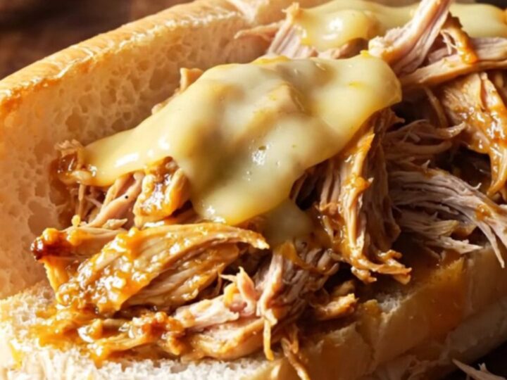 A close-up of shredded Mississippi chicken piled on a toasted hoagie roll with melted cheese.