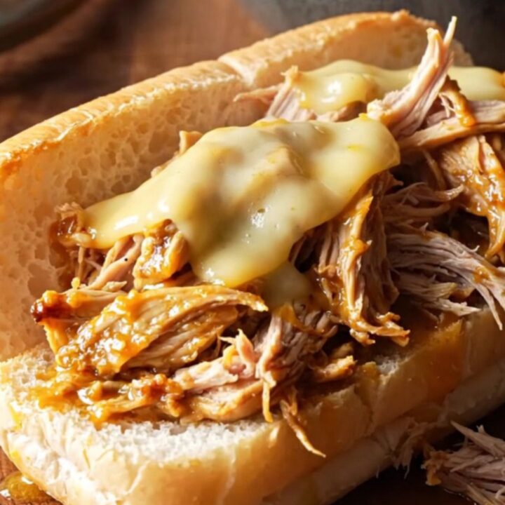 A close-up of shredded Mississippi chicken piled on a toasted hoagie roll with melted cheese.