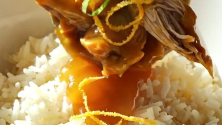 A close-up of shredded orange chicken in a glossy glaze served over jasmine rice.