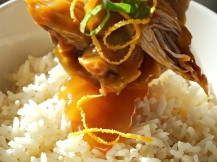 A close-up of shredded orange chicken in a glossy glaze served over jasmine rice.