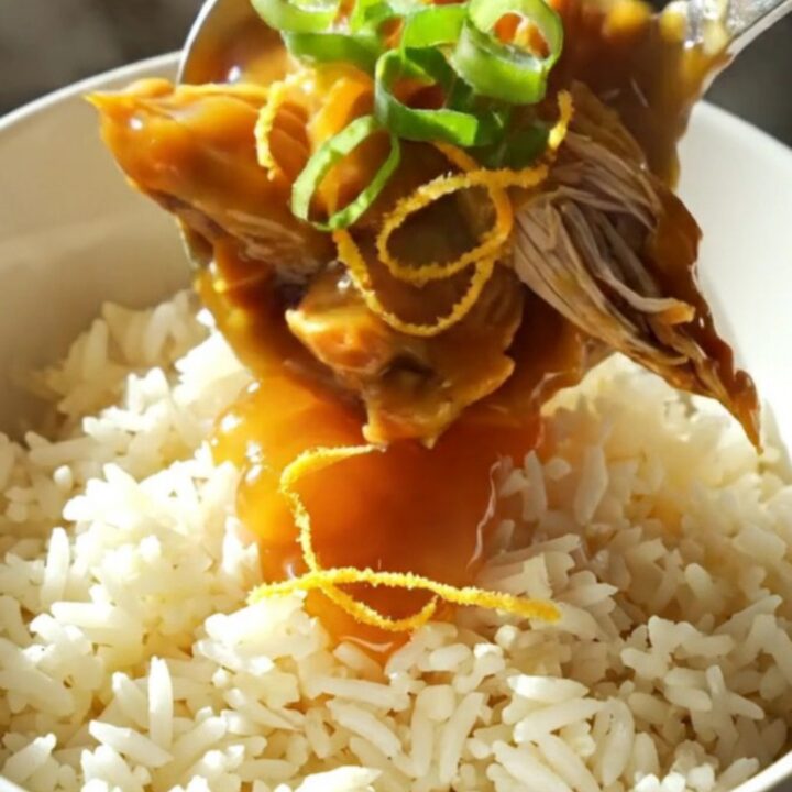A close-up of shredded orange chicken in a glossy glaze served over jasmine rice.