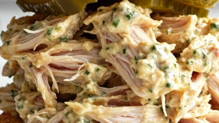 A close-up of shredded chicken in a creamy sauce inside a black ceramic slow cooker.