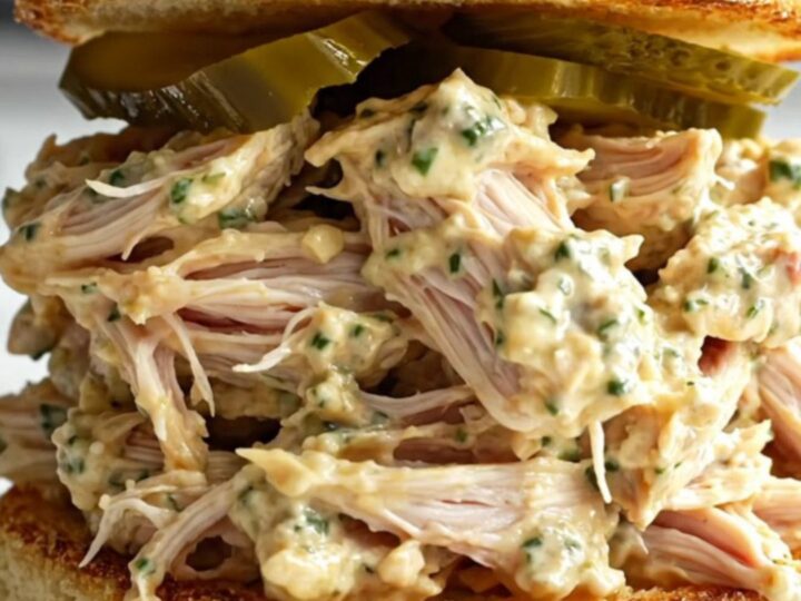 A close-up of shredded chicken in a creamy sauce inside a black ceramic slow cooker.