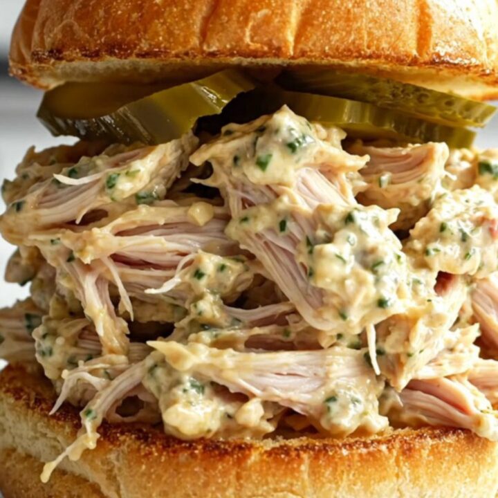 A close-up of shredded chicken in a creamy sauce inside a black ceramic slow cooker.