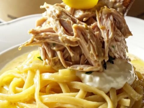 A close-up of tender shredded chicken in a creamy Dijon sauce with fresh tarragon in a cream-colored stoneware slow cooker.