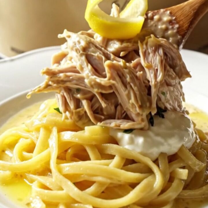 A close-up of tender shredded chicken in a creamy Dijon sauce with fresh tarragon in a cream-colored stoneware slow cooker.