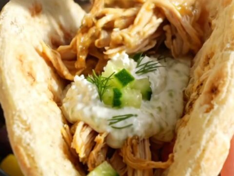 A close-up of shredded Greek lemon chicken with olives and feta in a blue-gray slow cooker.