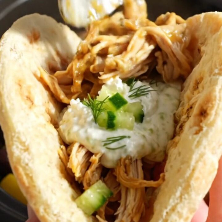 A close-up of shredded Greek lemon chicken with olives and feta in a blue-gray slow cooker.